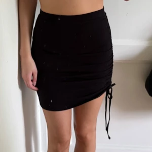 Svart kortkjol  - Supersnygg svart kortkjol från Even&Odd med tight passform och trendig snörning på sidan. Kjolen är i mjukt stretchigt material.