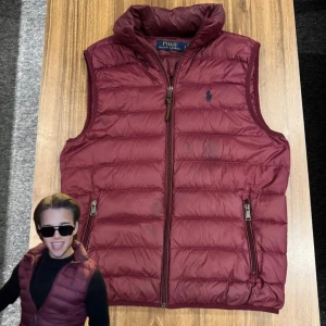 Ralph Lauren dunväst (Krobbes)  - Snygg vinröd dunväst från Polo Ralph Lauren med quiltad design och hög krage. Västen har två fickor med dragkedja och en diskret Polo-logga broderad på bröstet. Perfekt att slänga över en hoodie för extra värme under hösten och vintern. Synts med på några och Krobbes stora Tiktokvideos (exakt denna), är någon fläck på den. Annars väldigt bra skick! Storlek small. Nypris 3500kr, säljer för 1399kr! Allt gott, Brur!🫰🏽