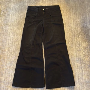 Lågmidjade svarta wide byxor med fickor - Snygga lågmidjade svarta byxor med breda ben och stora fickor framtill. Byxorna har låg midja och stängs med knapp och dragkedja. Perfekta för dig som gillar en avslappnad men trendig look. OBS! En liten smink fläck som syns på bilden, inte jätte synlig.