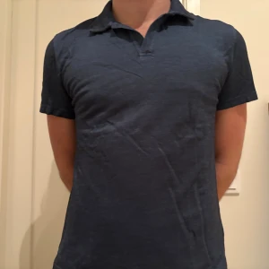 Mörkblå pikétröja från Oscar Jacobson - Snygg mörkblå pikétröja från Oscar Jacobson i klassisk modell med krage och korta ärmar. Tröjan är tillverkad i mjuk bomull och har en stilren look som passar perfekt till jeans eller shorts.