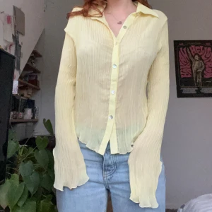 Super unik ljusgul blus  - Superfin ljusgul blus med plisserat tyg och genomskinlig look. Skjortan har långa ärmar, klassisk krage och pärlliknande knappar framtill. Materialet är lätt och flowy, perfekt för vår och sommar ✨
