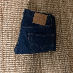 Levi's 501 mörkblå jeans W27 L28 - Klassiska Levi's 501 jeans i mörkblå denim med raka ben och snygga kontrastsömmar. Modellen har fem fickor och ikonisk läderpatch bak i midjan. Perfekta för dig som gillar tidlös stil och vill ha ett par jeans som alltid funkar.