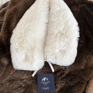 Vit  halsduk från Newport - Supermjuk och fluffig vit halsduk i fuskpäls från Newport. Halsduken har en klassisk form och knyts med ett vitt band framtill. Går att ha som huvud bonad eller detalj på jackor. Perfekt för att ge vinterlooken en lyxig och mysig touch. One size. Nypris runt: 1.000 sek