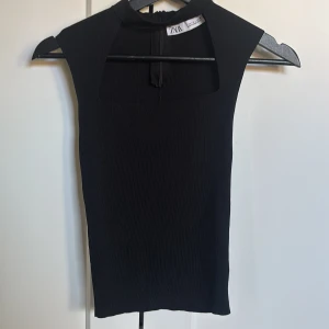 Svart ärmlös topp från Zara - Säljer en svart, ribbad ärmlös topp från Zara med fyrkantig ringning och dragkedja bak. Snygg och stilren modell som är lätt att matcha till olika outfits. Perfekt för dig som gillar minimalistisk stil.