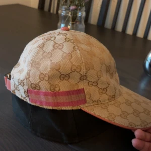 Keps - Säljer en keps som är beige med rosa detaljer på. Storlek M