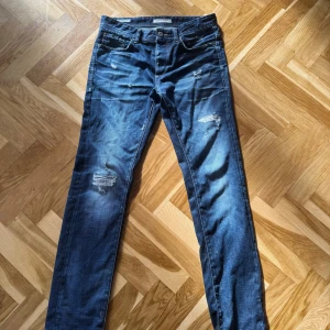 Blå slitna jeans från Jack and Jones med regular - Säljer ett par blå jeans från Jack and Jones (Nick/Regular Fit) med regular passform och slitna detaljer på låren och knäna. Storlek W30/L34