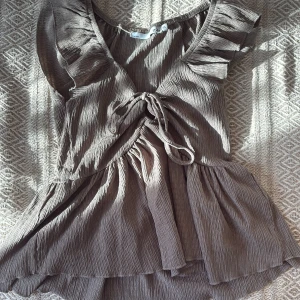 Brungrön ribbad blus med volang från Lager157💕 - Säljer en brun blus med ribbad struktur och volangkant nedtill. Toppen har v-ringning, snörning framtill och korta volangärmar som ger en söt och trendig look. Perfekt att styla med jeans eller kjol för en chill vibe. Från Lager157 i storlek XS💕