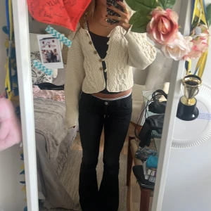 Beige stickad kofta med flätmönster - Superfin beige stickad kofta med snyggt flätmönster och träknappar. Koftan är croppad och har lång ärm, perfekt att slänga över ett linne. Mysig och trendig stil som passar till jeans eller kjol.