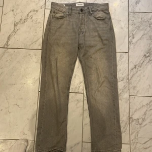 Grå jeans från Jack & Jones - Snygga grå jeans från Jack & Jones med klassisk femficksdesign och raka ben. Jeansen har en diskret tvättad look och är tillverkade i slitstarkt denim. Perfekta för dig som gillar en enkel och stilren vibe.