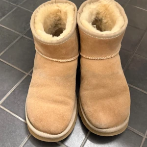 Beiga UGG boots i mocka - Beige uggs classic mini, använda i regn och snö därav skicket. Går att rengöra o få dom fina