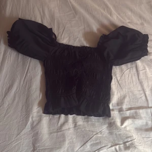 Svart offshoulder blus med puffärm - Supersöt svart blus med smockad kropp, volangkant nertill och puffiga offshoulder-ärmar. Typ magtröja 💕 oanvänd , nytt skick , ställ frågor om de behövs 💕