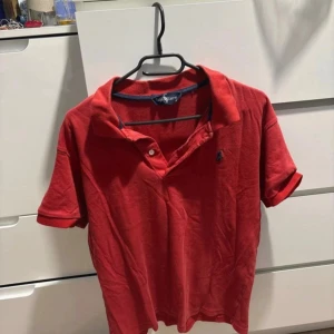 Röd polo t-shirt från Ralph Lauren - Riktigt snygg röd polo t-shirt från Ralph Lauren med klassisk krage och korta ärmar. T-shirten har den ikoniska broderade loggan på bröstet och är gjord i mjuk bomull. Perfekt för dig som gillar stilrena och tidlösa plagg. Priset går att diskutera