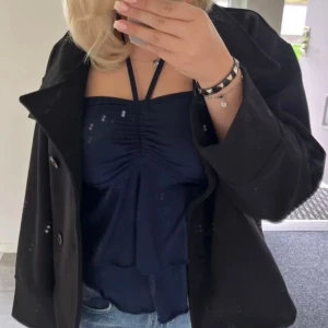 Mörkblå knyttopp - Säljer en mörkblå linnetopp med halterneck/knytband och snygg rynkning framtill. Toppen har volangdetaljer och öppen rygg med knyt i nacken. Storlek XS/S (lappen e bortklippt)