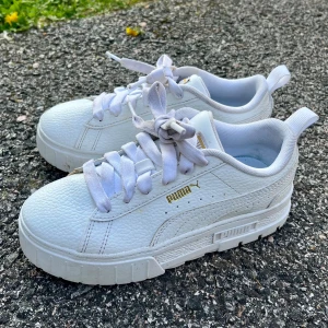 Vita Puma sneakers i skinn, strl 33 - Snygga vita Puma sneakers i skinn med chunky sula och gulddetaljer på sidan och plösen. Klassisk design med rund tå och breda vita snören. Perfekta för dig som gillar stilrena och sportiga skor med en modern touch.