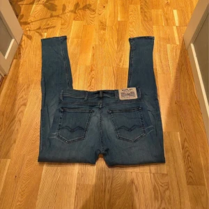 Replay Anbass - Snygga blå jeans från Replay med klassisk femficksdesign och diskreta slitningar. Jeansen har smal passform, normal midja och är tillverkade i stretchigt denim för extra komfort. Märkesdetaljer syns på bakfickan och myntfickan. W30 L32 fungerar lika bra för W29
