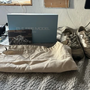 Philippe Model sneakers i mocka och mesh - Snygga Philippe Model sneakers i beige och vitt med detaljer i mocka och mesh. Skorna har snörning, rund tå och en ikonisk sköld på sidan med röd kant. Kommer med originalkartong och dustbag. Perfekta för dig som gillar stilrena och exklusiva sneakers. Är storlek 42 men skulle säga passar som 43or            Pris kan diskuteras!