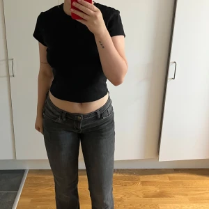 Gråa lågmidjade bootcut jeans - Säljer ett par gråa jeans med låg midja och bootcut-ben. Jeansen har klassiska fem fickor, bälteshällor och snygga sömdetaljer på bakfickorna. Perfekta för dig som gillar en avslappnad och trendig look.