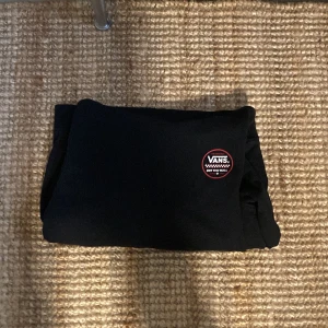 Svart sweatshirt från Vans - Svart sweatshirt från Vans med klassisk rund logga på bröstet i vitt och rött. Tröjan har en enkel och stilren design, perfekt för dig som gillar streetwear. Mjuk och skön bomullskvalitet.