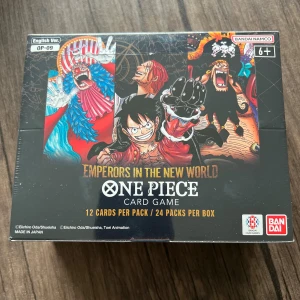 One Piece Card Game OP-09: Emperors in the New World.(English) - Samlarbox med One Piece-kortspel! Innehåller 24 booster packs med 12 kort i varje, fyllda med episka karaktärer som Luffy, Gol D. Roger och Nami. Perfekt för fans av manga, anime och strategiska kortspel. Skapa din egen piratbesättning och utmana vänner!