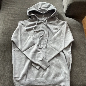 Ljusgrå cashmir hoodie med huva och snörning - En stilren ljusgrå hoodie med huva och snörning. Tröjan har långa ärmar och ribbade muddar vid ärmslut och nederkant. Perfekt för en avslappnad look och enkel att matcha med jeans eller joggers.