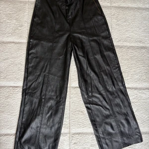 Svarta vida byxor i skinnimitation XS - Snygga svarta byxor från Gina Tricot i skinnimitation med vida ben och hög midja. Byxorna har dekorativa sömmar framtill och dragkedja i sidan, sitter snyggt! Kortare modell, passar mig som är ca 160cm. 