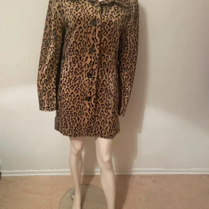 Leopardmönstrad satinrock med knappar - Snygg rock i leopardmönster med glansig satinfinish. Jackan har klassisk krage, raka långa ärmar och stängs med svarta knappar framtill. Perfekt statement-plagg för dig som vill sticka ut och addera lite edge till din outfit.