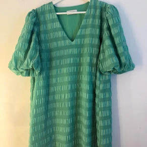 Modström klänning  - Grön klänning med V-ringning och puffärmar. Klänningen har ett horisontellt randigt mönster. Mycket fint skick. Nypris: 1300kr. Storlek L