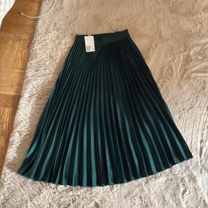 Mörkgrön plisserad långkjol H&M - Supersnygg mörkgrön plisserad långkjol från H&M i storlek 34. Kjolen har ett brett midjeband och ett elegant fall.