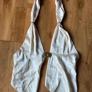 Vit topp med snäckspänne - Supersnygg vit top med halterneck och ett unikt snäckformat spänne framtill. 