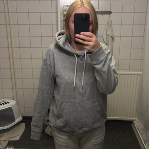 Grå hoodie från H&M med huva - Enkel och stilren grå hoodie från H&M i storlek S. Tröjan har huva med snörning, magficka och långa ärmar. Perfekt för chill dagar eller när du vill ha något bekvämt och snyggt. Materialet är mjuk bomullsblandning.