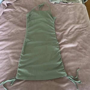 Grön ribbad halterneckklänning Shein - Snygg ljusgrön ribbad klänning från Shein i halterneckmodell med knytband i nacken och på sidorna. Klänningen är kroppsnära och har en kort längd, perfekt för varma dagar. Materialet är mjukt och stretchigt för en bekväm passform.