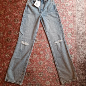 Never Denim ljusblå wide jeans W24 L32 - Ljusblå jeans från Never Denim i modellen JP Regular Wide 570. Hög midja och raka, vida ben med slitna detaljer på knäna. Klassisk femficksmodell i bomullsdenim med dragkedjegylf och knapp. Perfekta för en avslappnad och trendig look. Nypris 599kr