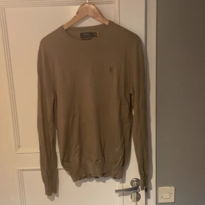 Beige merinoullströja Polo Ralph Lauren - Snygg beige långärmad tröja från Polo Ralph Lauren i tvättbar merinoull. Slim fit-modell med rund hals och diskret broderad logga på bröstet. Perfekt för dig som gillar stilrena och klassiska plagg med en lyxig känsla. Obs liten fläck på bröst men inget man tänker på där av priset.