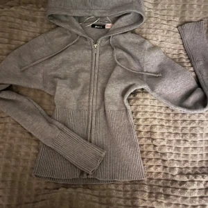 hoodie gina - Mysig grå stickad hoodie från Gina Tricot med dragkedja framtill och huva med snörning. Tröjan är otroligt mjuk och  har långa ärmar och ribbade muddar samt midja för en snygg passform. Perfekt för kyliga dagar och enkel att matcha med jeans eller leggings.