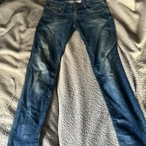 Blå Replay jeans, midwaist, storlek 28/30 - Snygga blå jeans från Replay med klassisk femficksdesign och diskreta slitningar framtill. Modellen har normal passform och raka ben. Jeansen är tillverkade i mjukt denimtyg som sitter skönt hela dagen. Perfekta för dig som gillar stilrena och tidlösa jeans.