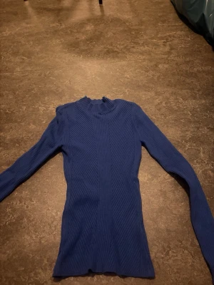 Blå ribbstickad tröja med lång ärm - Säljer en blå ribbstickad tröja med lång ärm och rund hals. Tröjan har en smal passform och är tillverkad i ett mjukt, stretchigt material som sitter snyggt på kroppen. Perfekt att styla med jeans eller kjol för en trendig look.