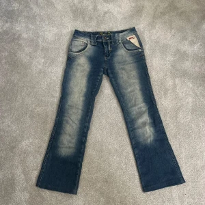 Miss Isi bootcut jeans med broderi - Snygga blå bootcut jeans från Miss Isi med coolt broderat hjärta på bakfickan och slitna detaljer framtill. Klassisk femficksmodell med kontrastsömmar och låg midja.  Hittar ingen storlek men passar mig som har xs-s och är 161 och har sprättat upp sömen där nere så att de blir lite längre men det syns inte.