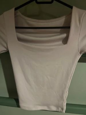 Ljusrosa croppad topp med kort ärm - Säljer en ljusrosa croppad topp med korta ärmar och bred, fyrkantig urringning. Toppen är tight i modellen och gjord i mjukt bomullsmaterial. Perfekt att styla med höga jeans eller kjol.