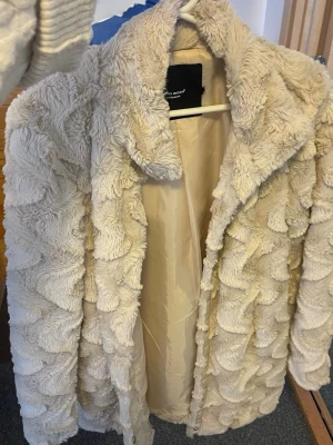 Beige fluffig pälsjacka från Vero Moda - Säljer en supermjuk och fluffig beige pälsjacka från Vero Moda. Jackan har ett vågigt mönster i fuskpäls, bred krage och helfoder på insidan. Perfekt för dig som vill ha en varm och trendig look under kalla dagar.