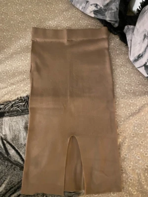 Beige/ ljus brun ribbad långkjol med slits - Säljer en mörk beige/ljus brun långkjol i ribbat material. Kjolen har en snygg slits baktill som ger extra edge till outfiten. Perfekt att styla med en croppad topp eller oversized tröja. Midjemodell med stretchig passform.
