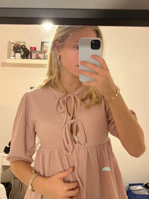 Ljusrosa blus med knyt fram - Söt ljusrosa blus med två knyten framtill. Blusen har lite längre ärm och är gjord i ett mjukt, strukturerat tyg. Från lager 157, använd 1-2 gånger🥰