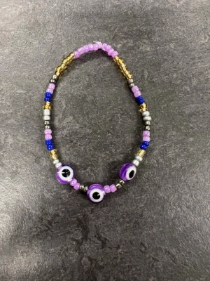 Färgglatt pärlarmband storlek M  - Armband med pärlor i lila, blått, guld och silver samt tre större lila ögonpärlor. 
