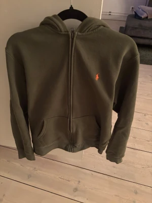Olivgrön hoodie från Polo Ralph Lauren - Snygg olivgrön hoodie från Polo Ralph Lauren med dragkedja framtill. Tröjan är barn storle L passar ungefär som en xs. Tröjan är sparsamt använd. Priset är ej hugget i sten, hör av er vid frågor!