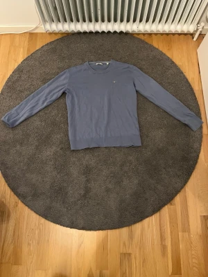 Blå långärmad tröja från Gant - Snygg blå långärmad tröja från Gant med rund halsringning och diskret logga på bröstet. Tröjan har en klassisk passform och är tillverkad i ett mjukt, tunt material som passar perfekt till lager på lager. Enkel och stilren design.