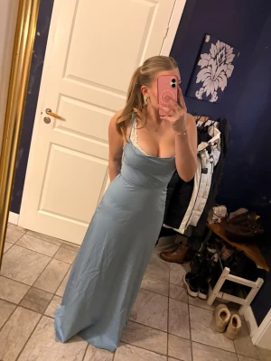 Ljusblå långklänninh i satinlikt material - Snygg ljusblå långklänning med smala axelband. Klänningen har en knytning i ryggen och är tillverkad i ett glansigt satinliknande material. Perfekt för bal. Från NA-KD