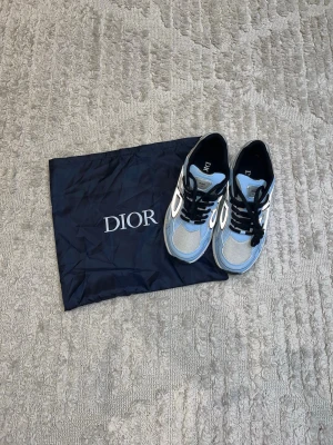 Dior sneakers i blått och vitt - Snygga Dior sneakers i blått, vitt och svart med meshpaneler och detaljer i läder. Klassisk låg modell med svarta skosnören och vit sula. Perfekta för dig som vill ha en exklusiv och trendig look.