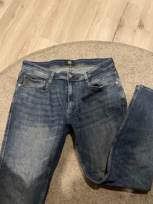 Blå jeans från American Classic Jeans - Snygga blå jeans från American Classic Jeans, modell 521. Jeansen har klassisk femficksdesign, raka ben och är gjorda i slitstark denim. Perfekta för dig som gillar en tidlös och avslappnad stil.