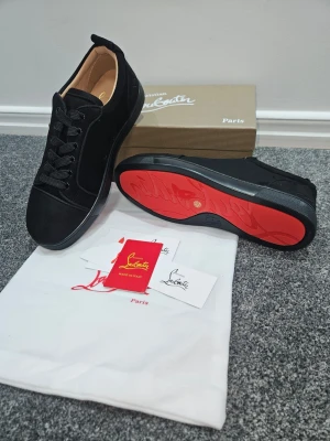 Svarta Louboutin sneakers med röd sula - Snygga svarta sneakers från Christian Louboutin i mocka med klassisk röd sula. Lågt skaft, svarta skosnören och diskreta detaljer. Insidan är beige och skon har en exklusiv känsla. Perfekta för dig som vill sticka ut med stil.