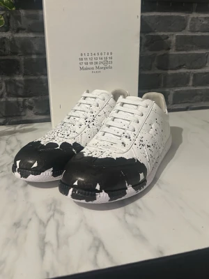 Svart-vita Maison Margiela Gats - Unika vita Maison Margiela Gats med svart färgstänksdesign över tå och sidor. Klassisk låg modell med vita skosnören och sula. Aldrig använda! Priset är ej hugget i sten vid snabb affär! Postar inom 24h✅