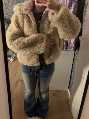 Beige fluffig fur jacks - Supermjuk och fluffig teddyjacka i beige färg med dragkedja framtill och stor krage. Jackan är croppad och har en oversized passform som ger en chill vibe. Perfekt för kalla dagar när du vill vara både varm och snygg.
